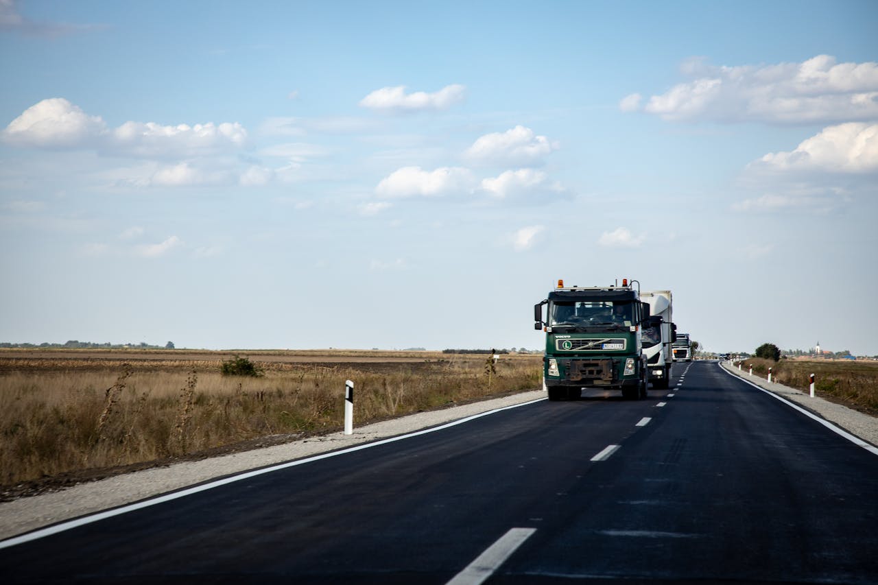 Rural highway with trucks driving under blue skies and scattered clouds.